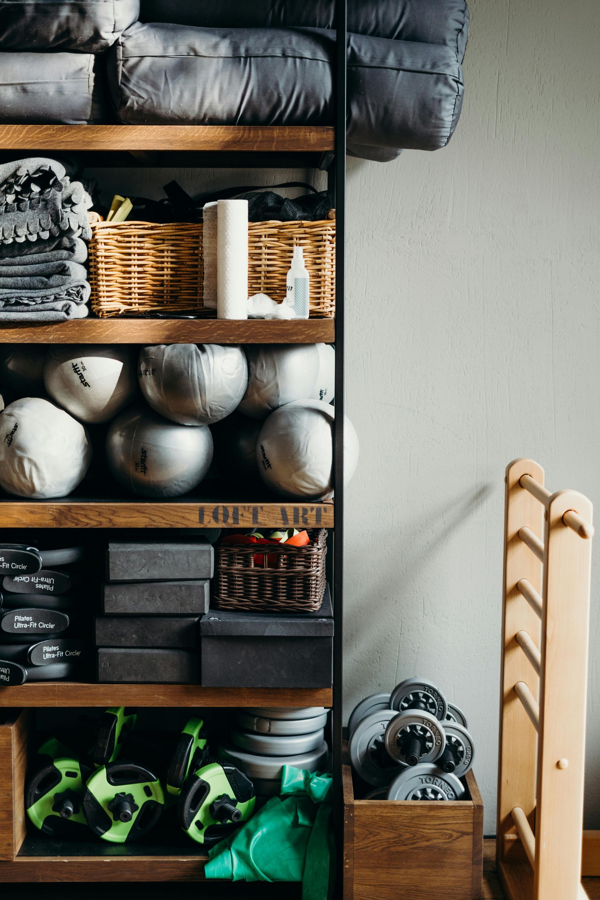 Shelves of rolled mats, baskets, and yoga props beside a wooden ladder in a studio corner