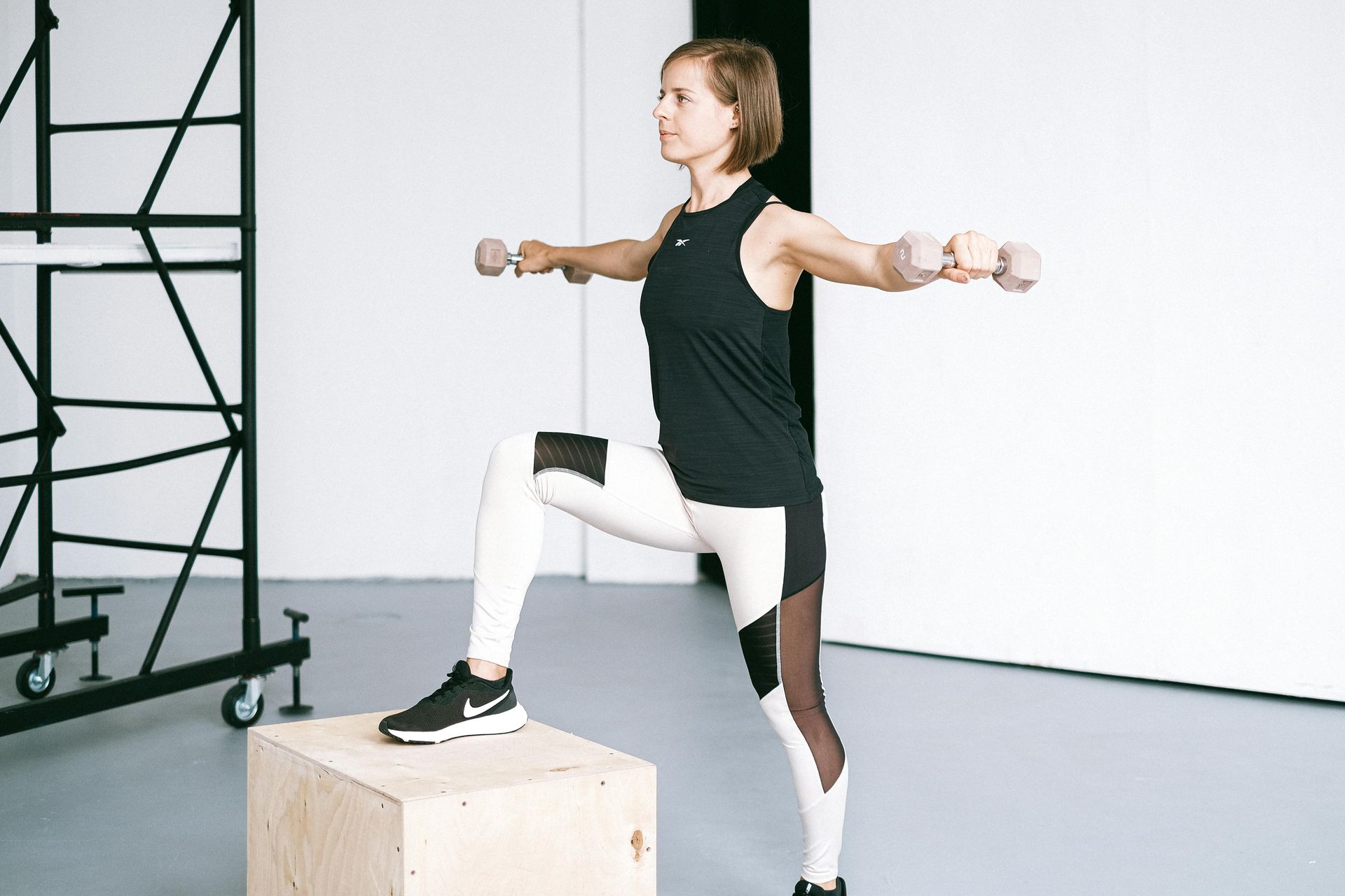 Person balancing on a wooden box while holding dumbbells in a gym-like studio