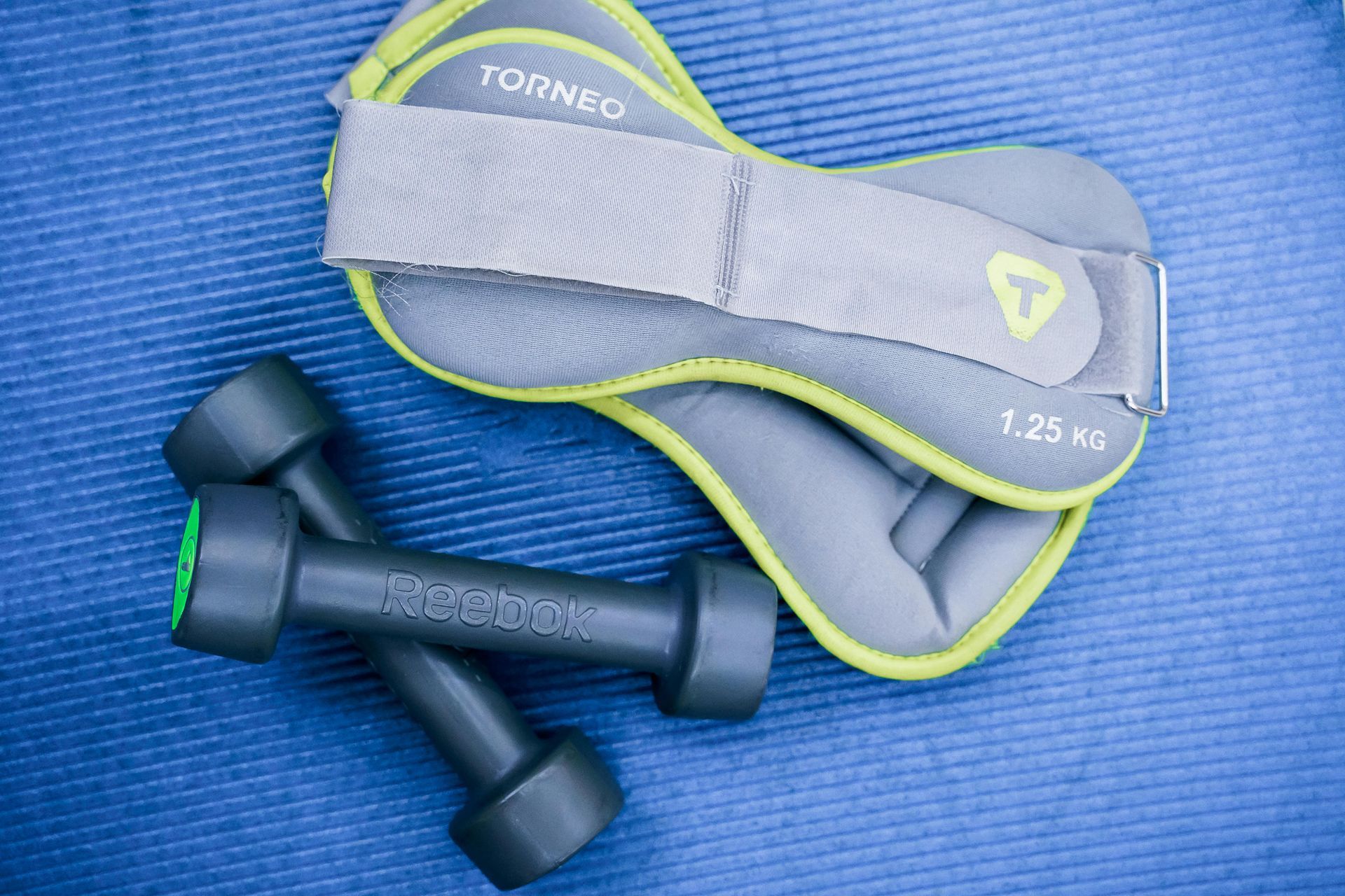 Gray and lime-green ankle cuff with black exercise handles on a blue mat