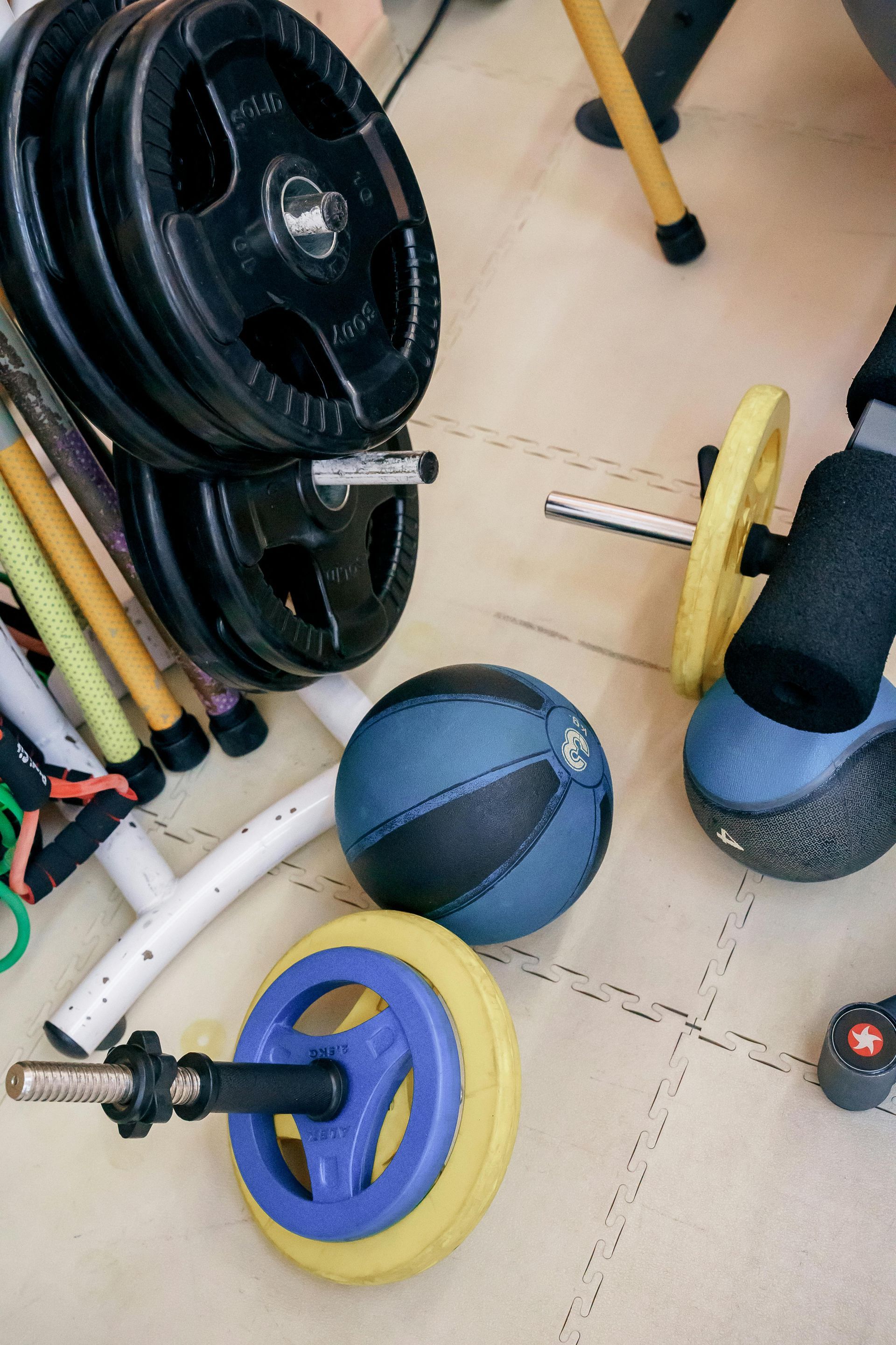 Gym equipment and weight plates scattered on a floor, including a blue medicine ball and barbell with yellow plates