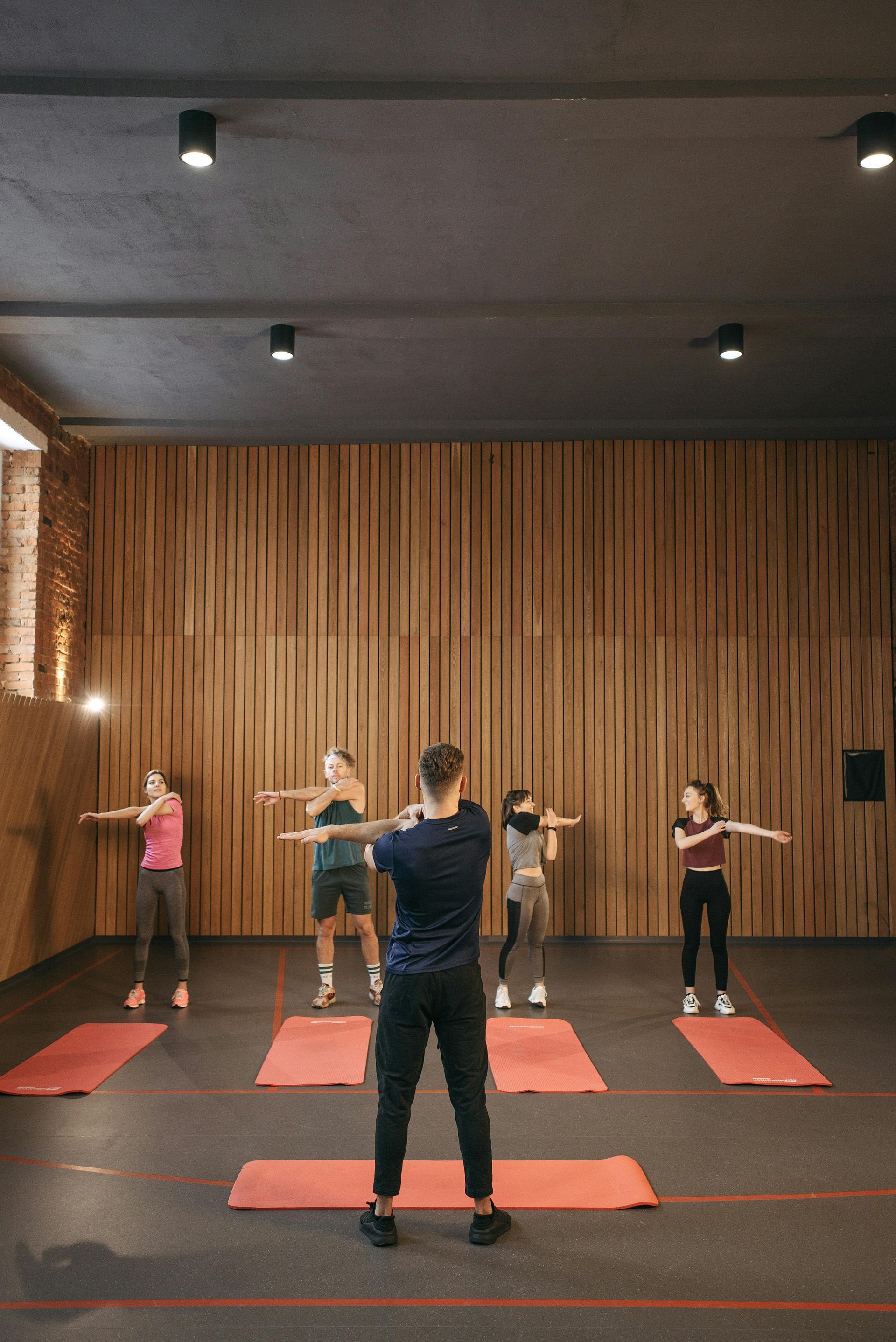 People practicing yoga on red mats in a studio with wooden slat wall and overhead lights