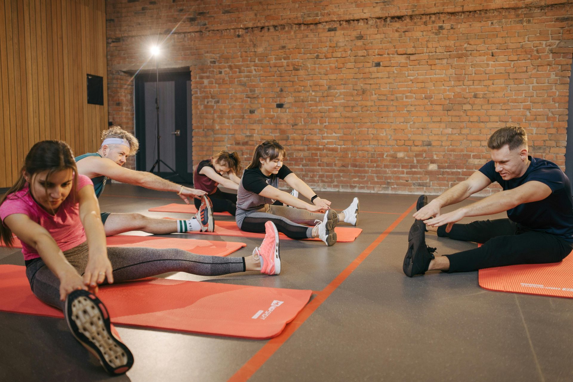 People stretching on mats in a brick-walled fitness studio