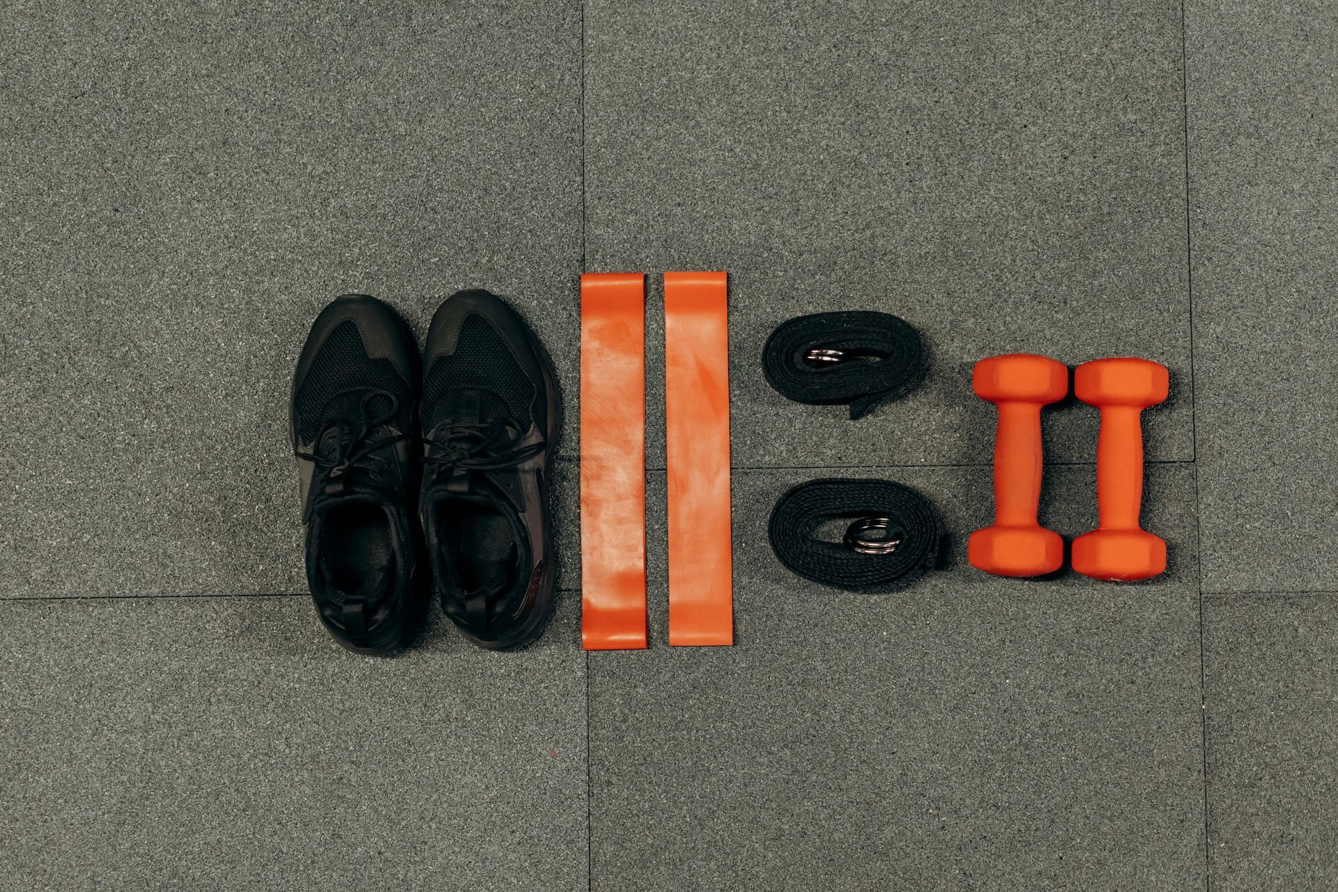 Black shoes, orange reflective bands, and orange dumbbells arranged on a gray floor.