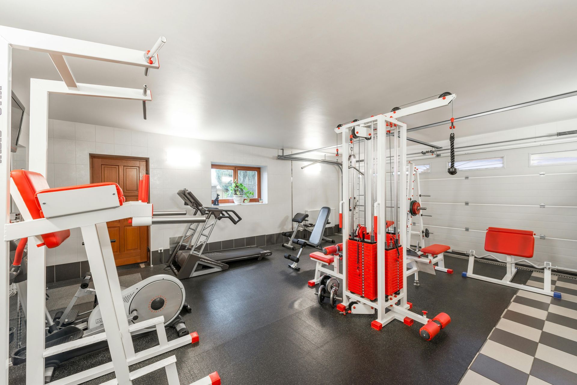 Bright home gym with red-and-white exercise machines, mirrors, and black rubber flooring