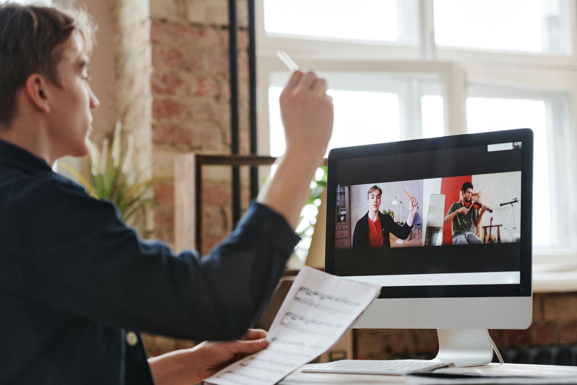 Person conducting a video meeting at a desk, viewing a split-screen call on a desktop monitor.