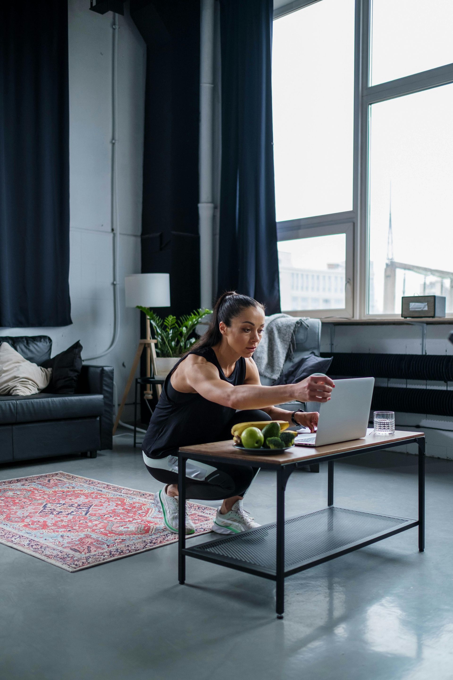 Woman eating at a coffee table in a bright living room with large windows