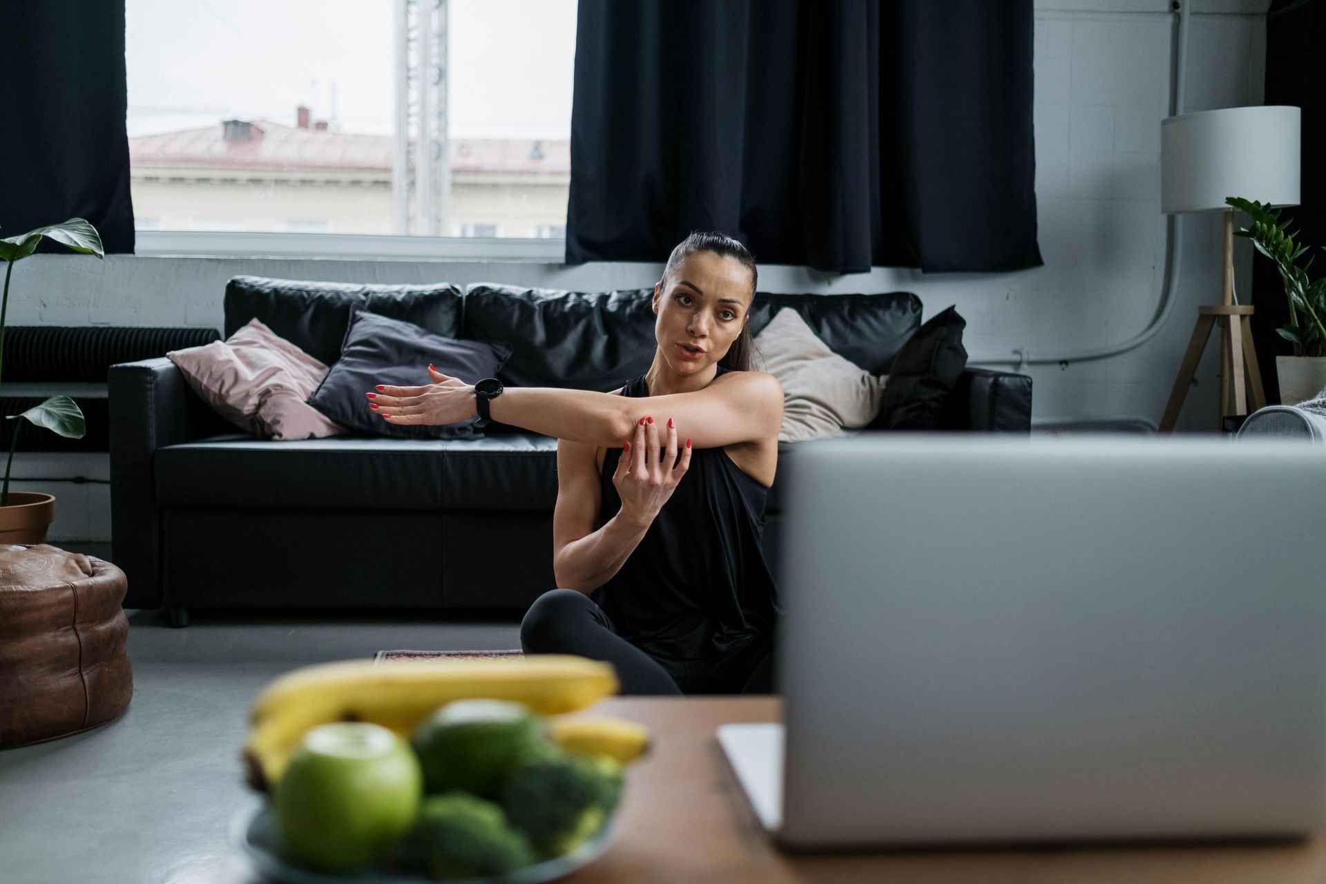 Person sitting on a living room floor behind a laptop, with fruit in the foreground and a sofa in the background
