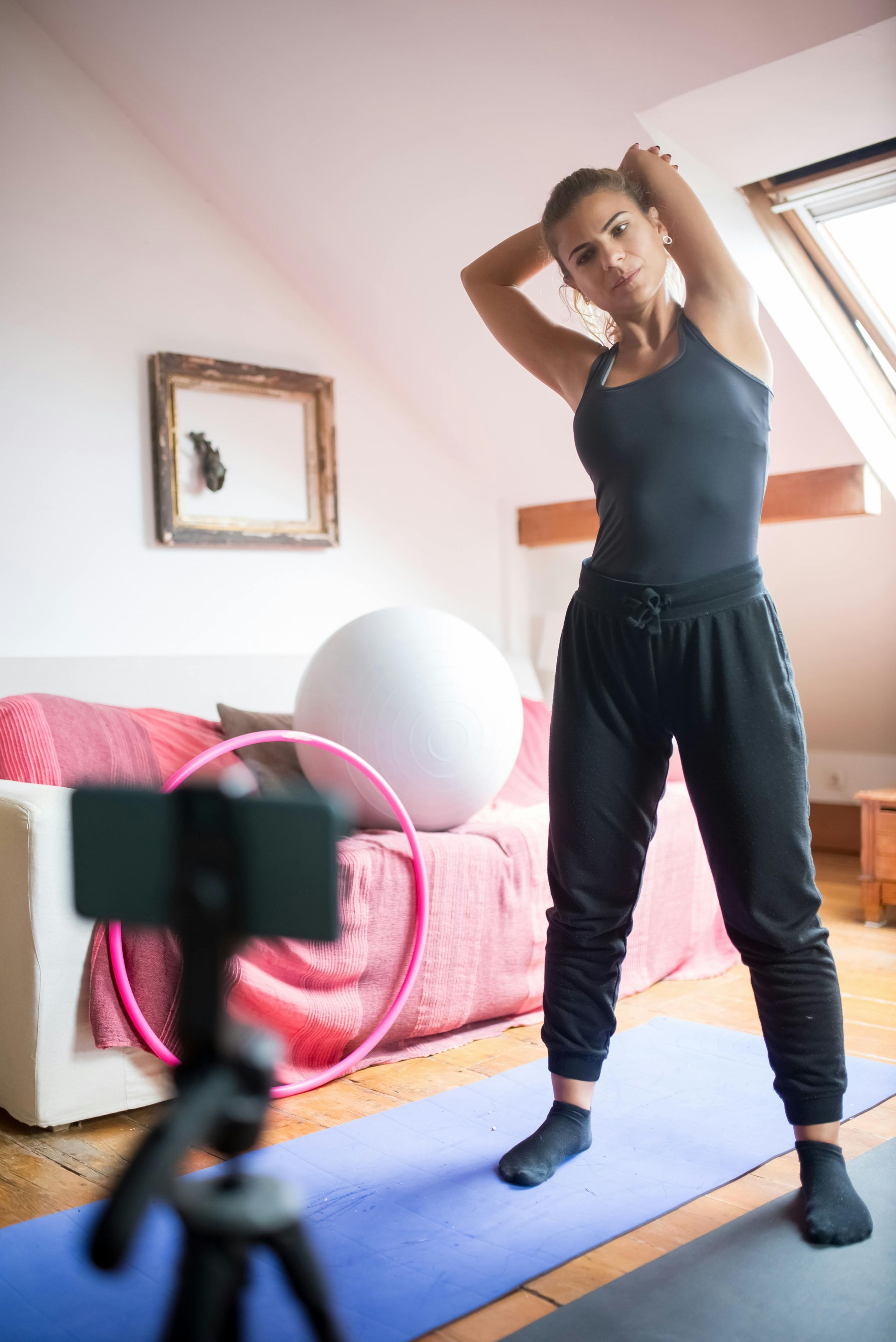 Person stretching on a yoga mat in a living room, with a camera on a tripod in the foreground