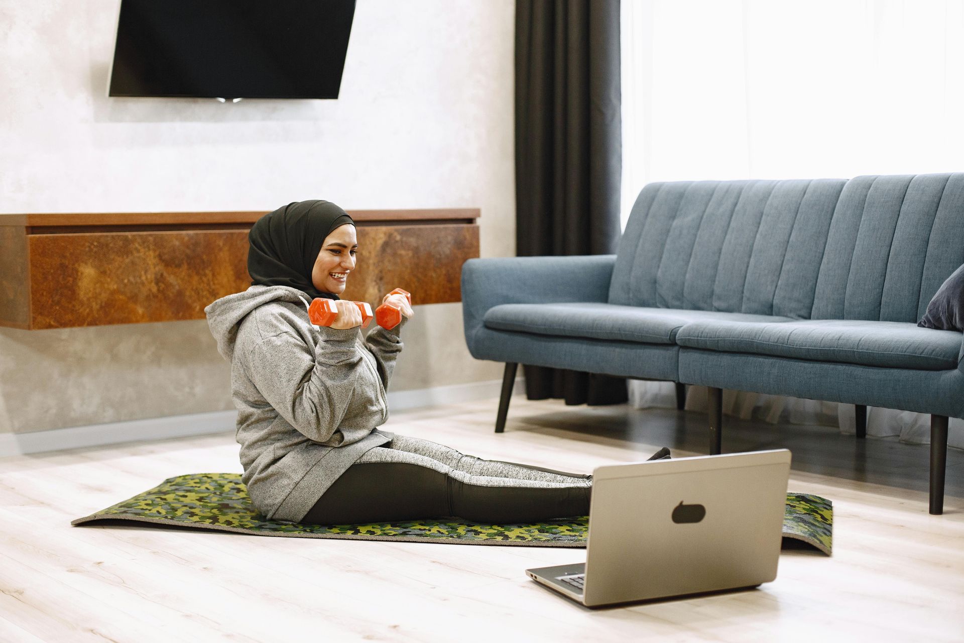 Person sitting on a rug with a laptop, holding a small flower pot in a modern living room