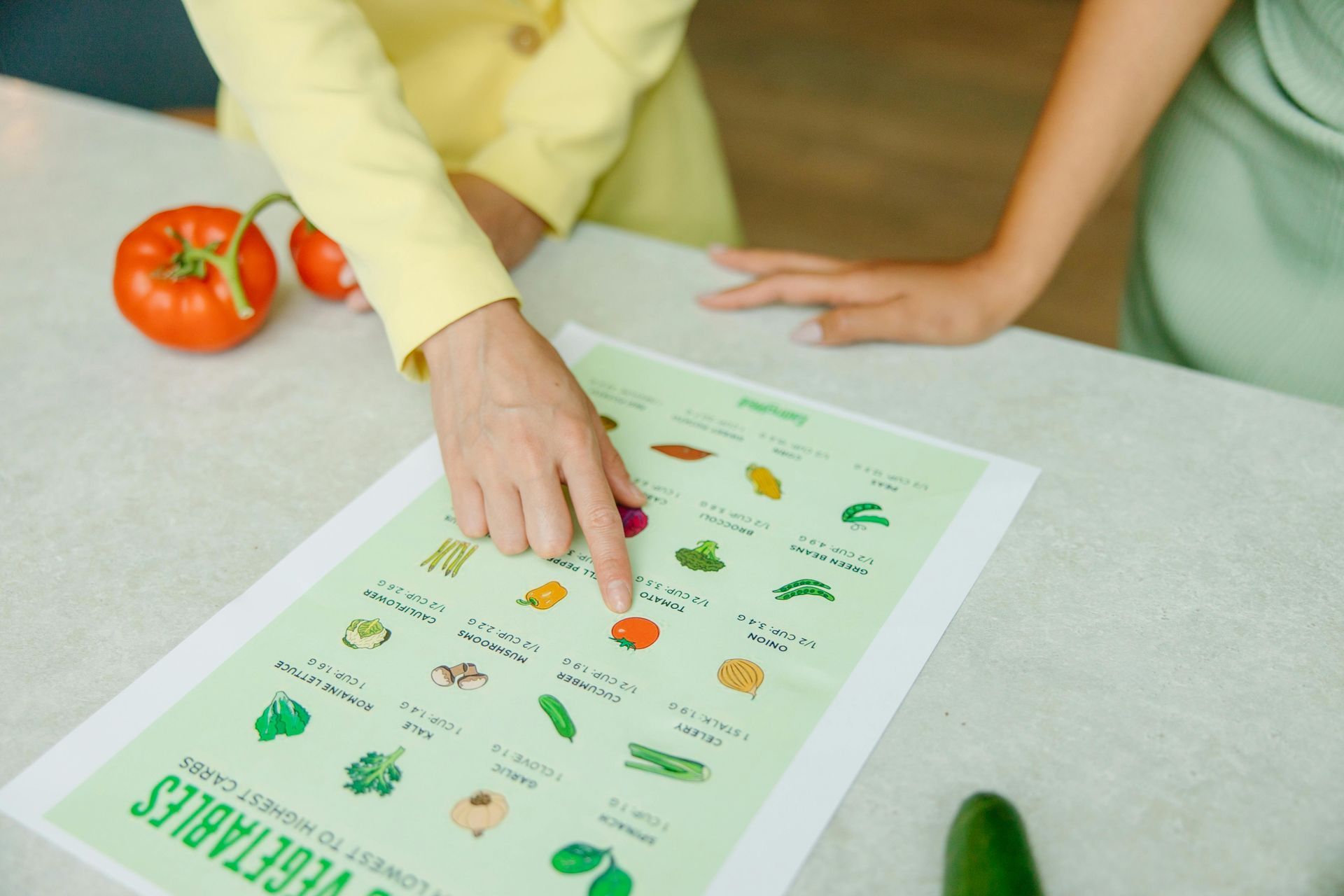 Hands pointing at a green eco guide on a table with tomatoes and cucumber nearby