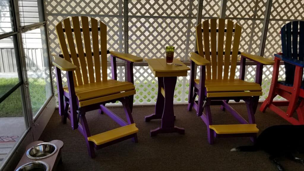 A screened in porch with yellow and purple chairs and a table.