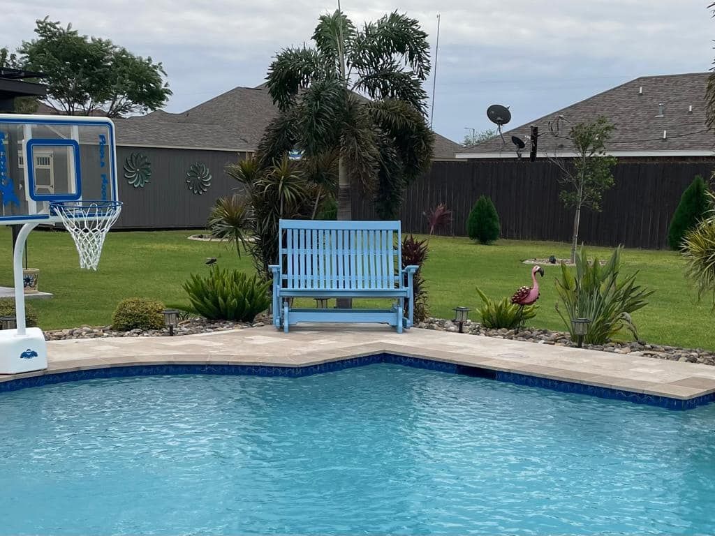 A blue bench sits next to a swimming pool with a basketball hoop in the background