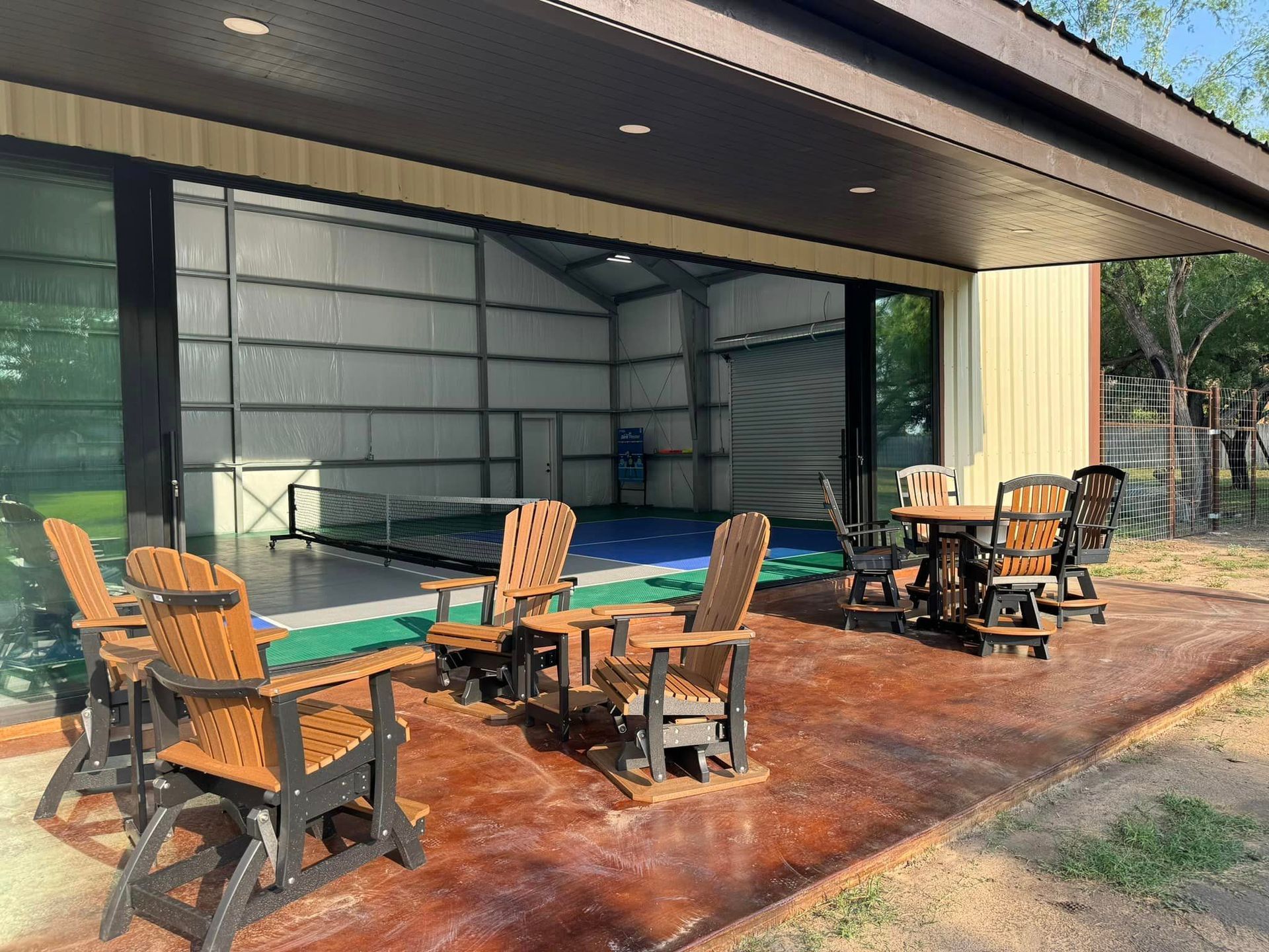 A patio with chairs , tables and a pool in the background.