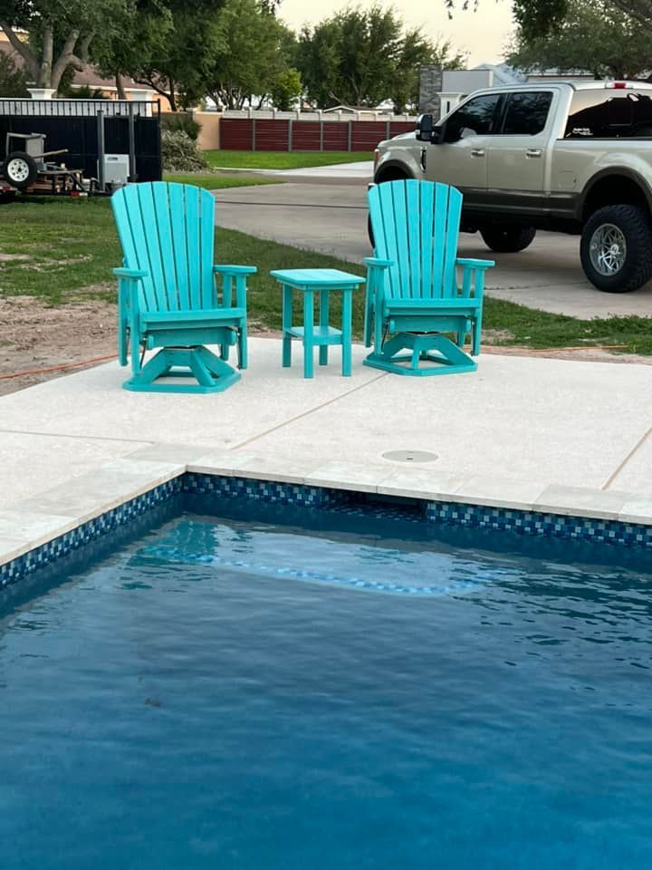Two blue adirondack chairs sit next to a swimming pool