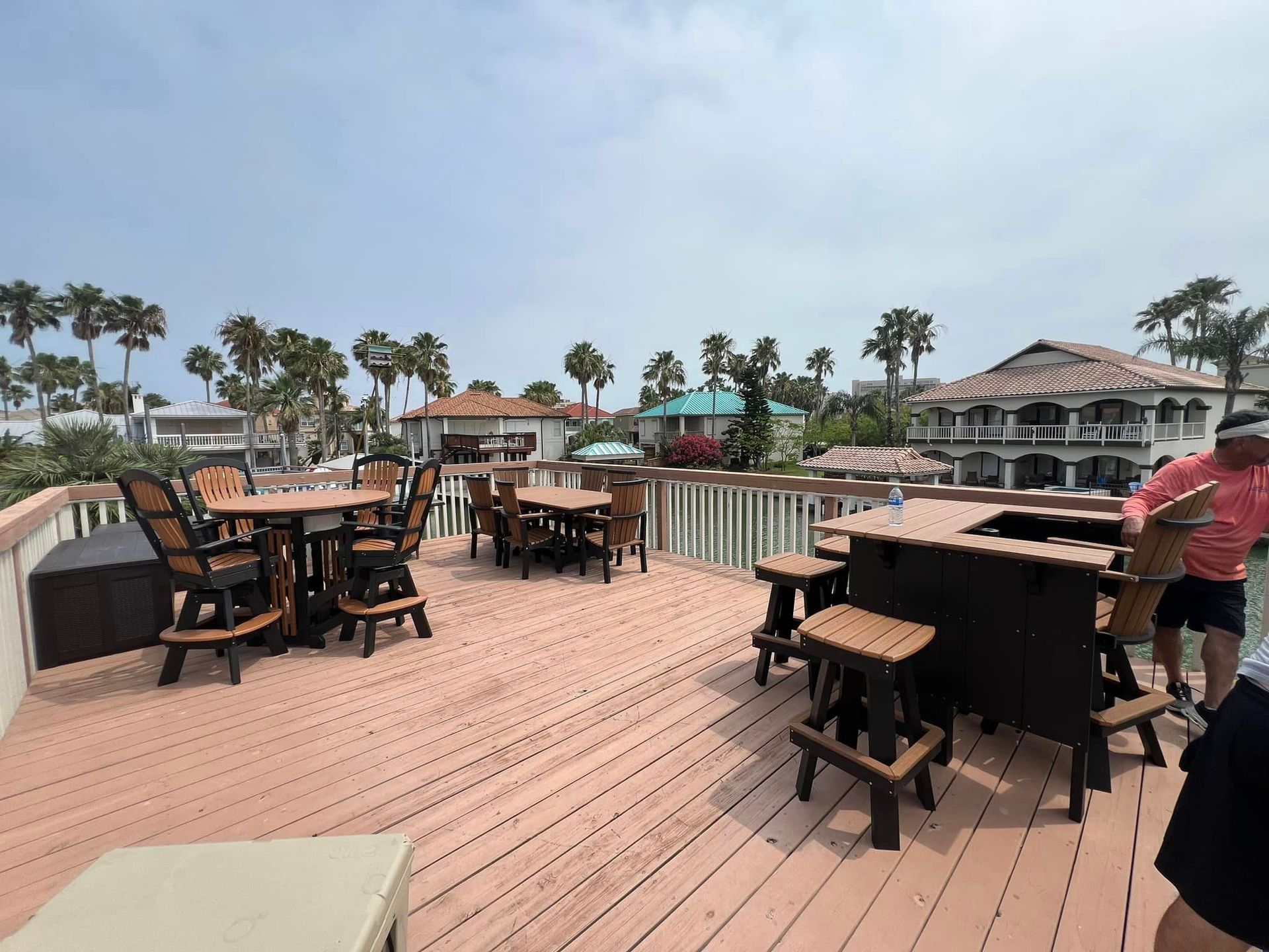 A man is standing on a deck with tables and chairs.