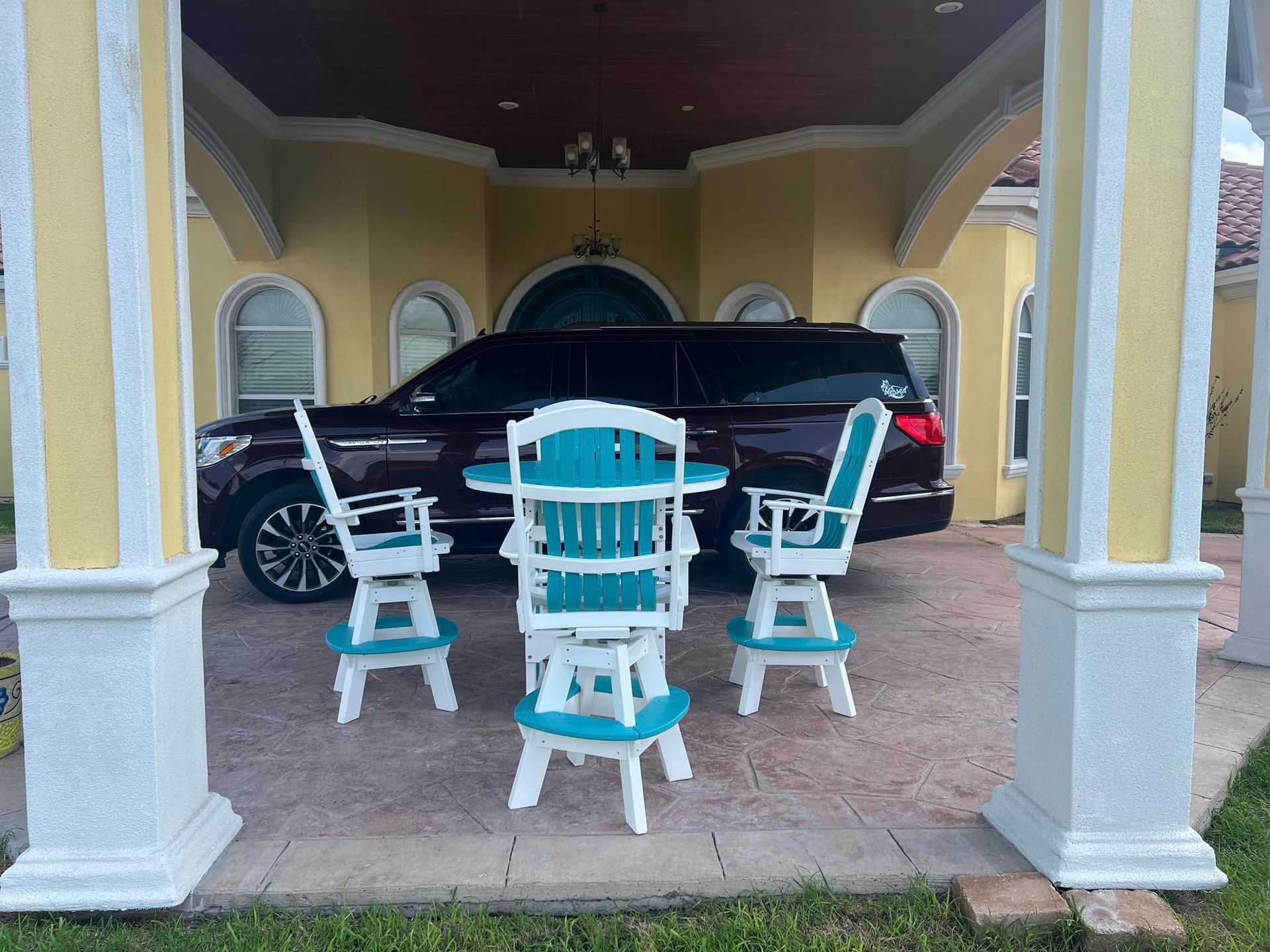 A car is parked under a gazebo next to a table and chairs.