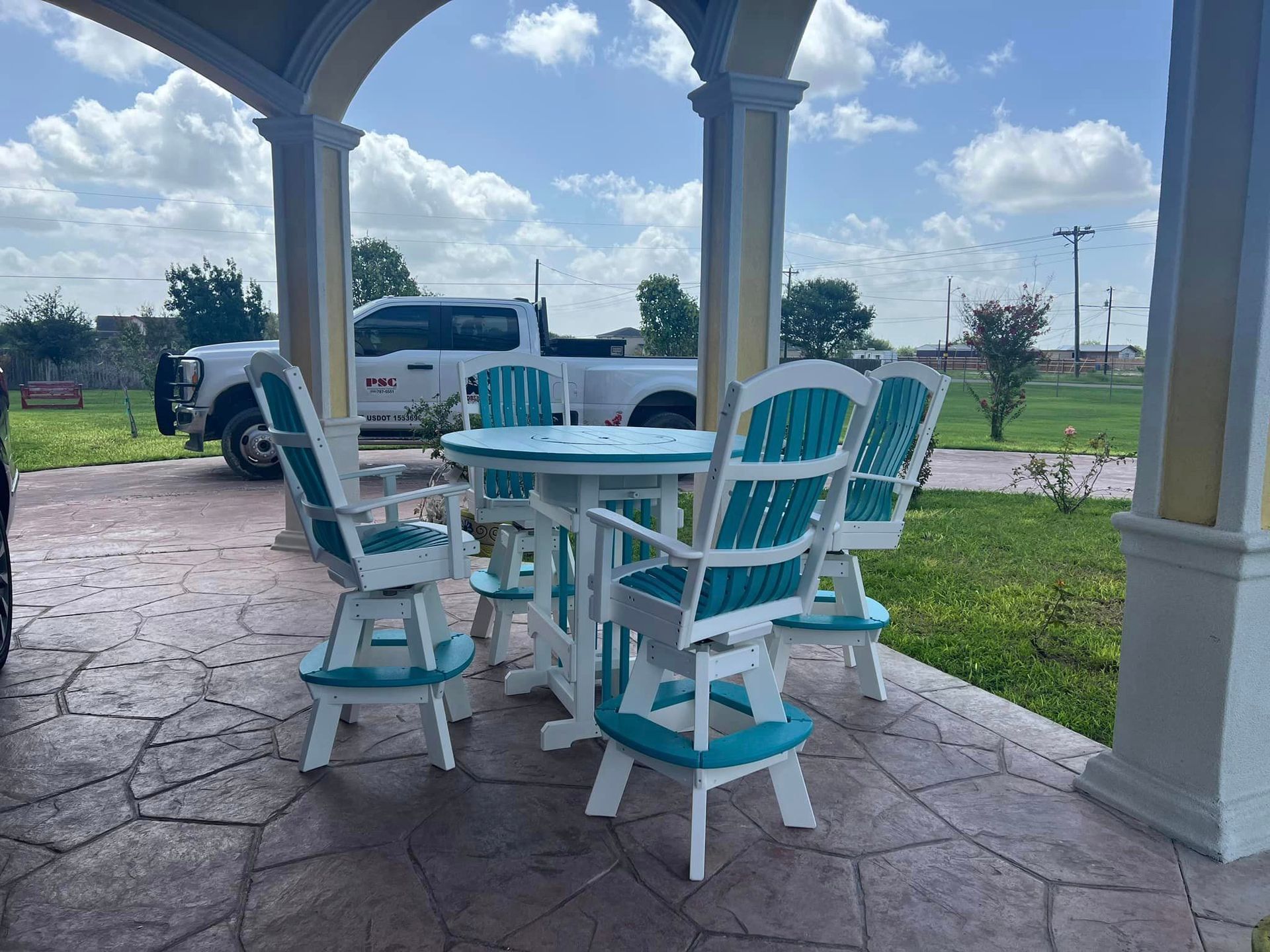 A patio with a table and chairs and a truck parked in the background.