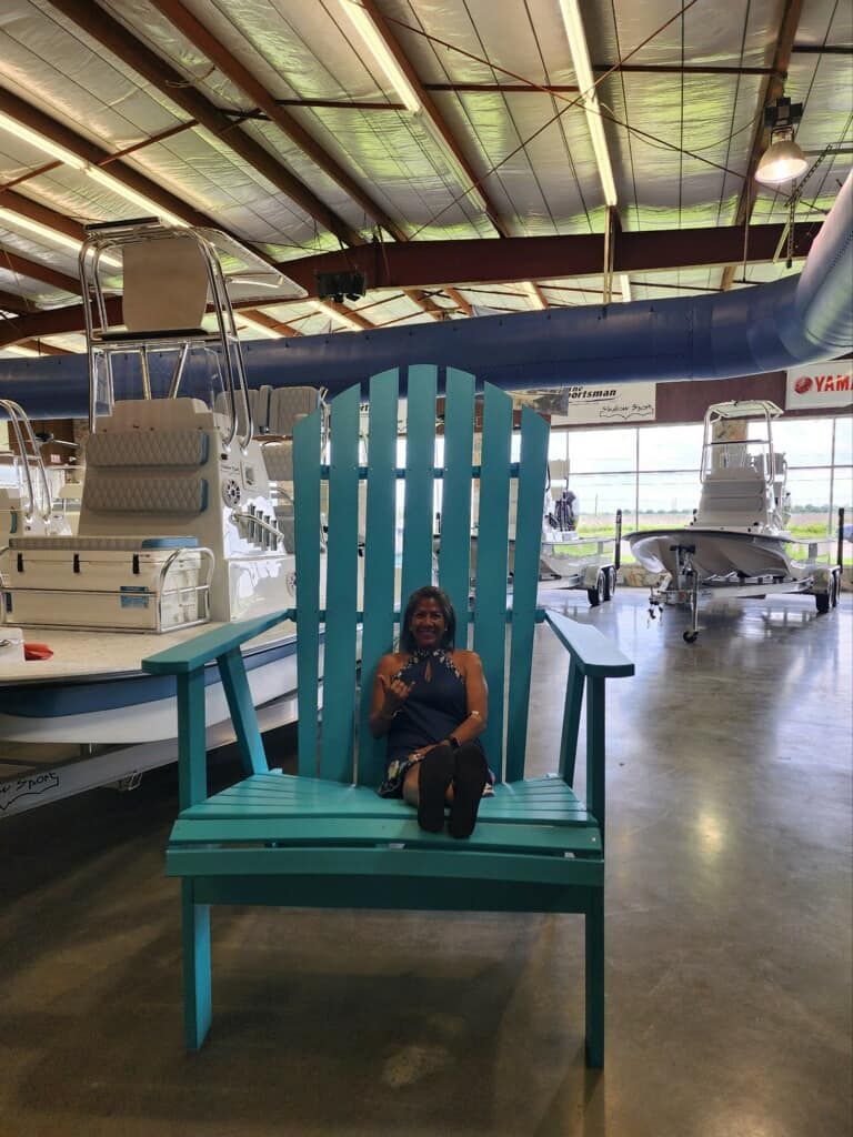A woman is sitting in a large blue chair in a boat showroom.