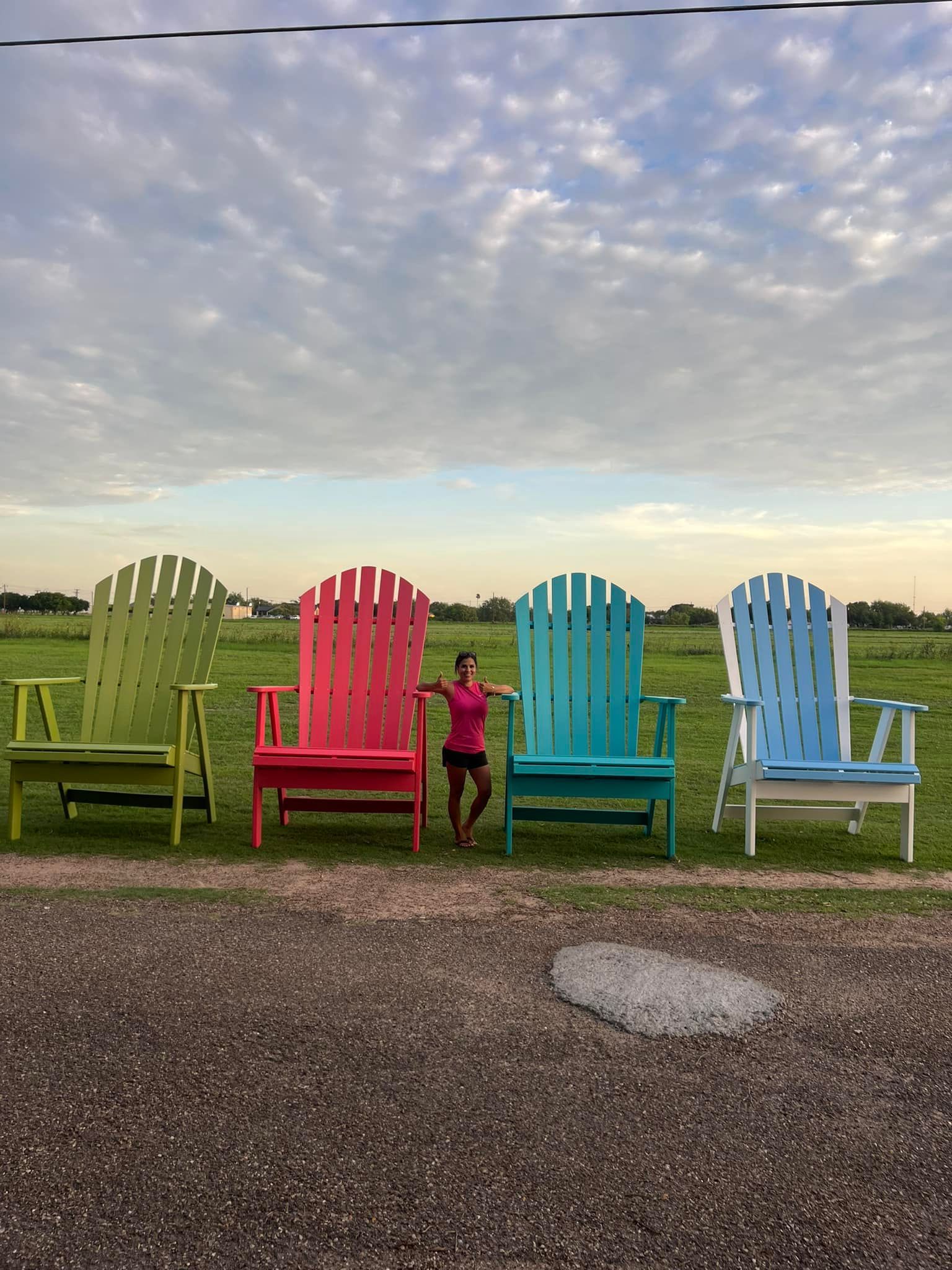 A girl is standing in front of a row of colorful adirondack chairs.
