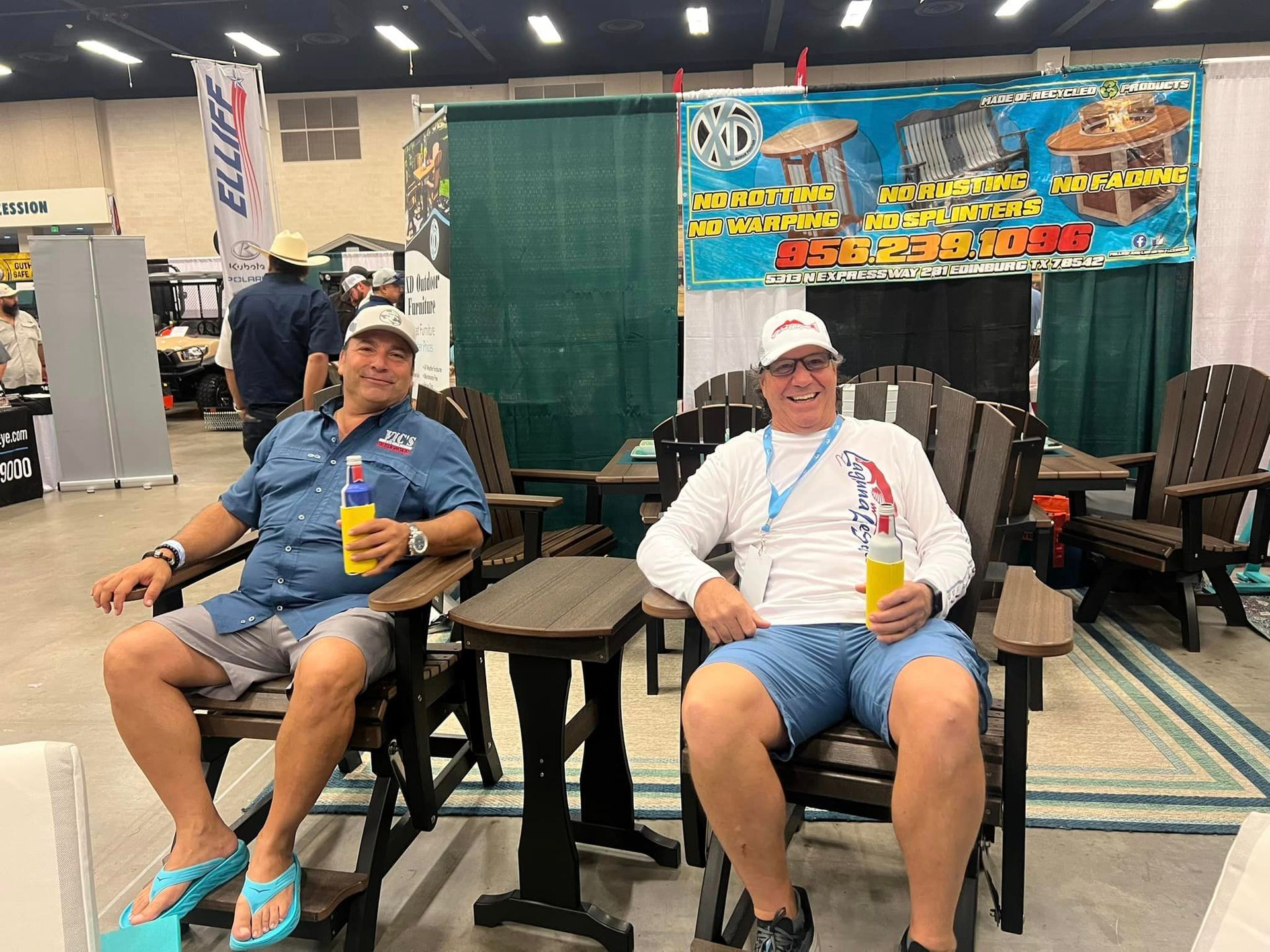 Two men are sitting in chairs at a convention holding drinks.