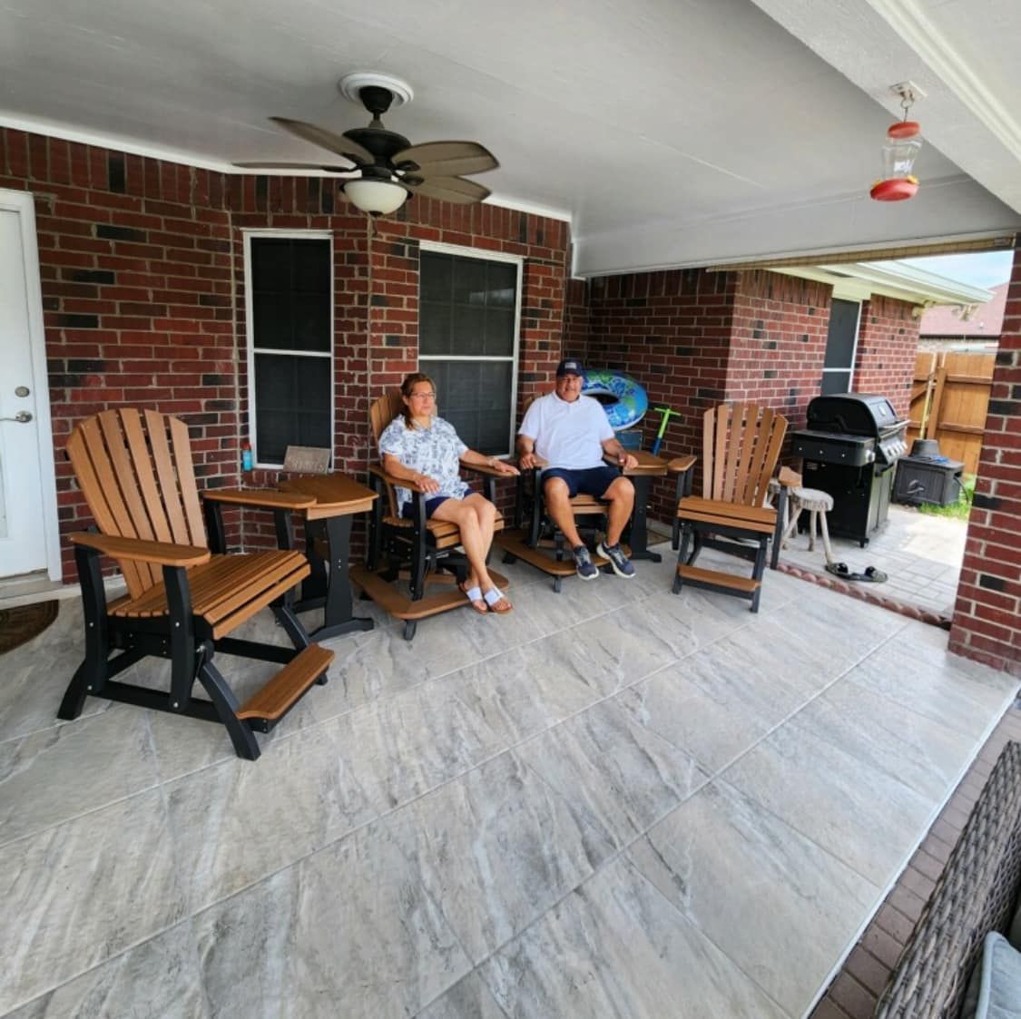 Two people are sitting on a porch with a ceiling fan