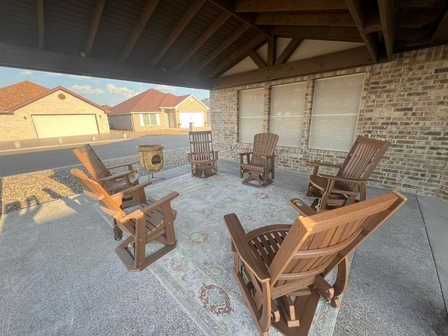 A group of wooden rocking chairs are sitting under a covered patio.
