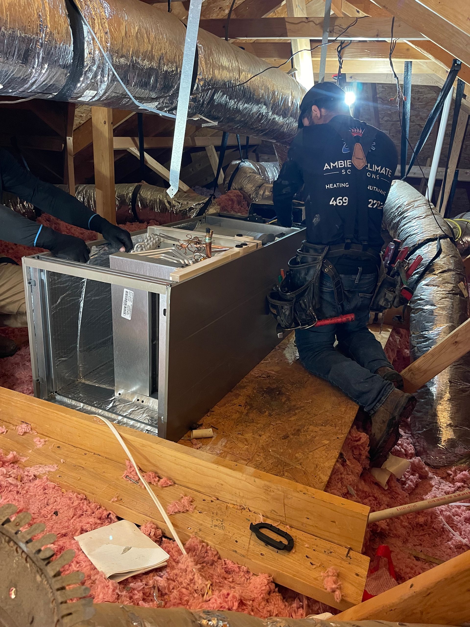 A man is working on an air conditioner in an attic.
