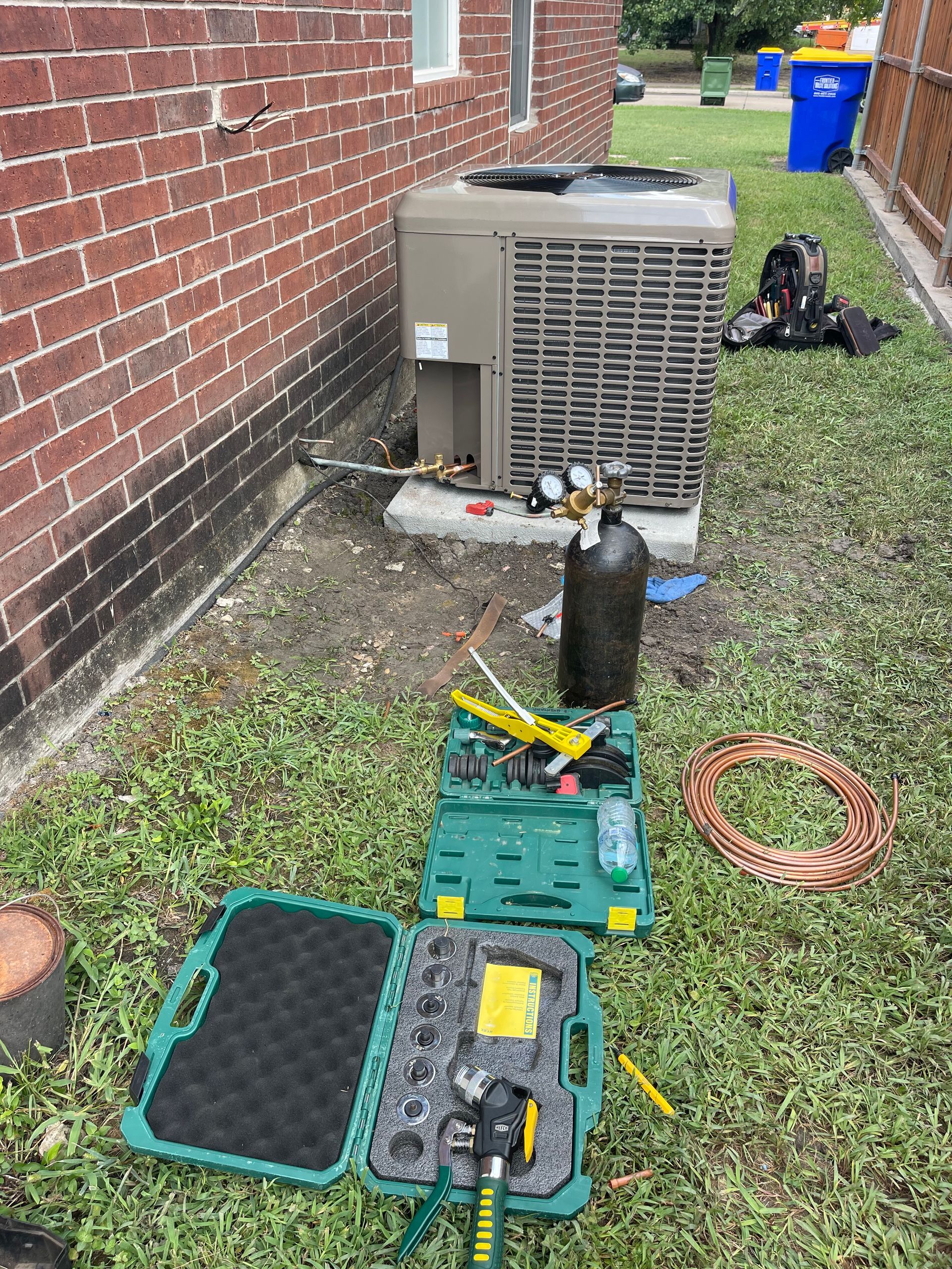 An air conditioner is being repaired in the backyard of a house.
