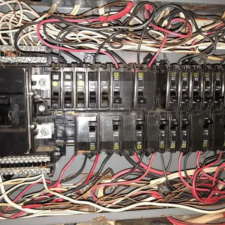 Electrical panel with numerous wires and circuit breakers.