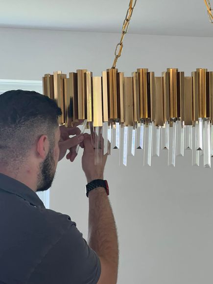 Man adjusting a gold chandelier with hanging glass rods, indoors.
