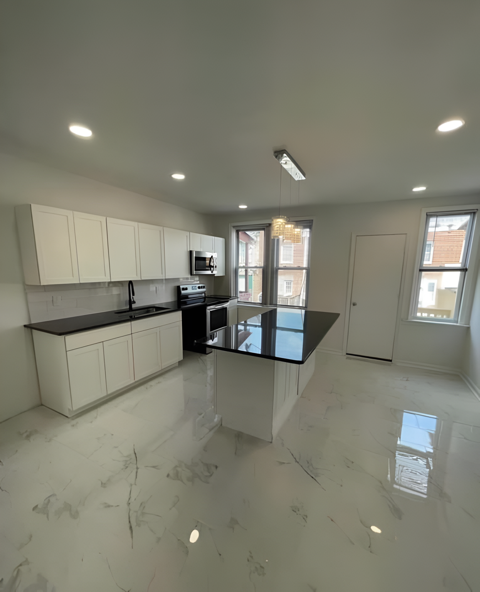 Modern white kitchen with black countertops, island, and appliances. Bright, open space with marble-look flooring.