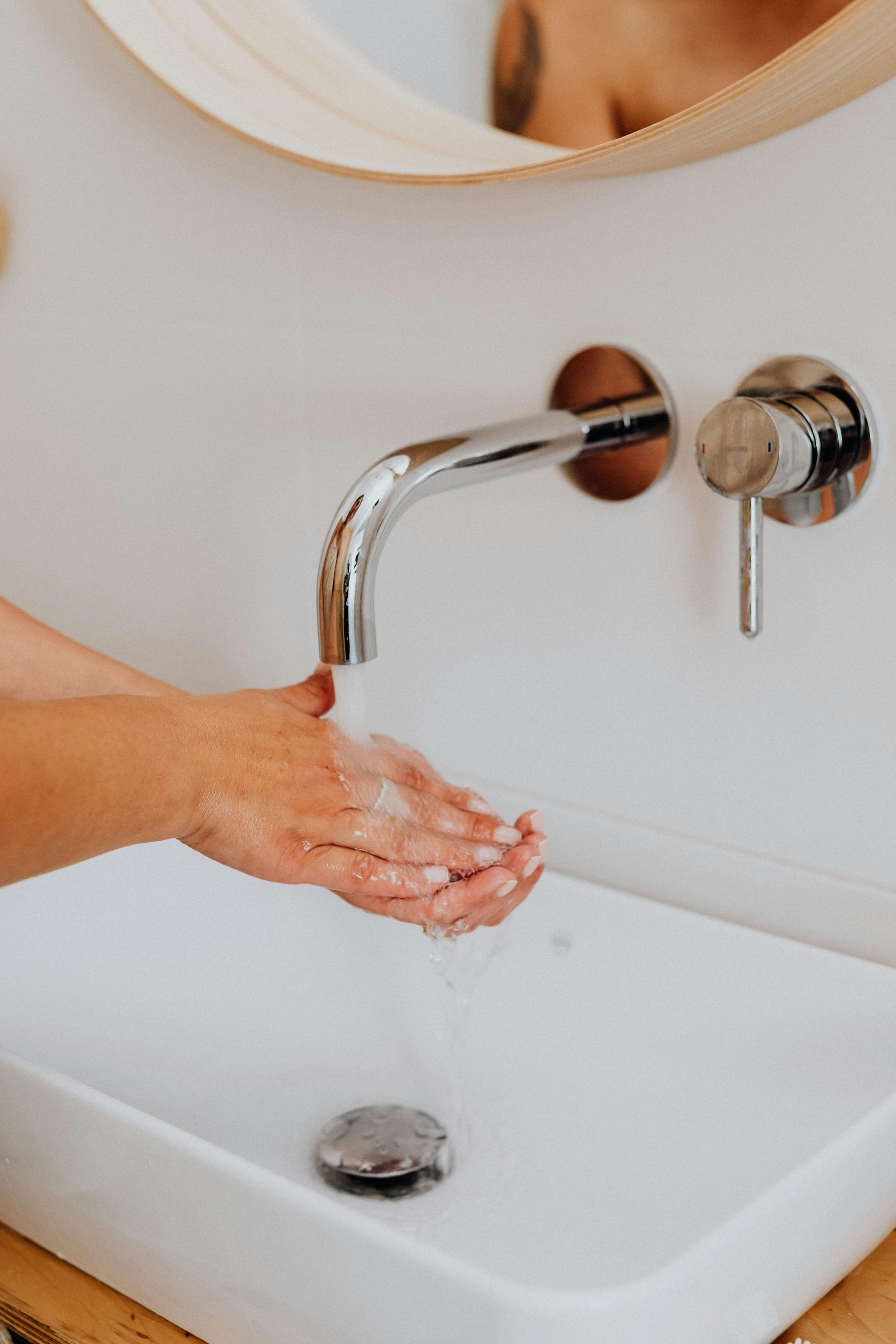 Person washing hands with soap under a chrome faucet in a white sink.