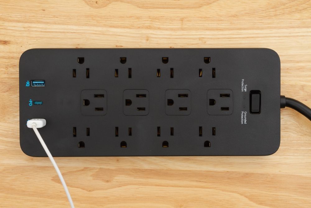 Black power strip with multiple outlets and USB ports, plugged in.