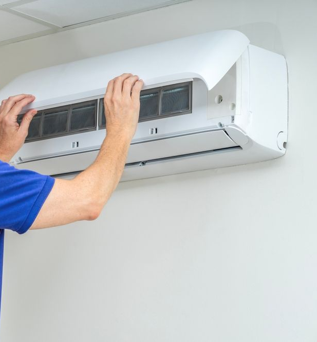 Person cleaning an air conditioner filter. White unit on a white wall.