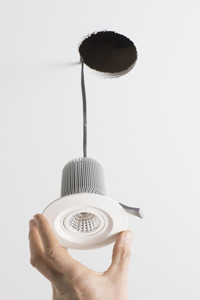 Hand installing a recessed ceiling light into a circular hole, white ceiling.