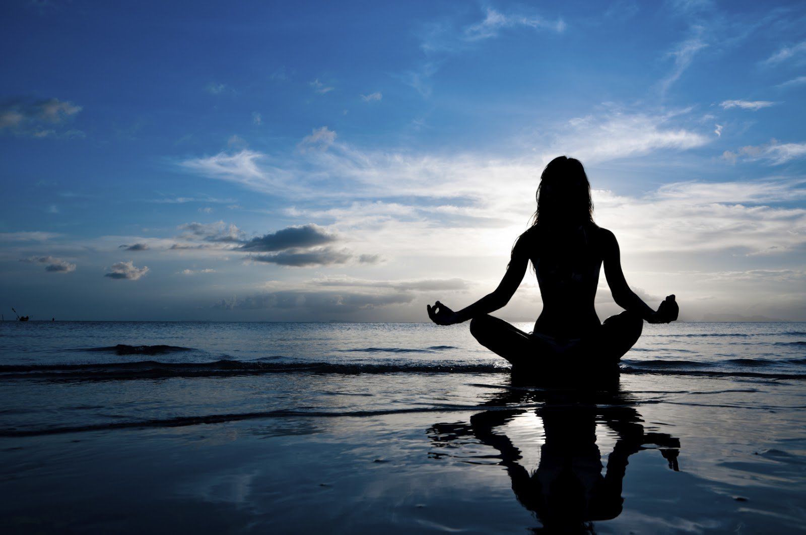 a woman is sitting in a lotus position on the beach at sunset .