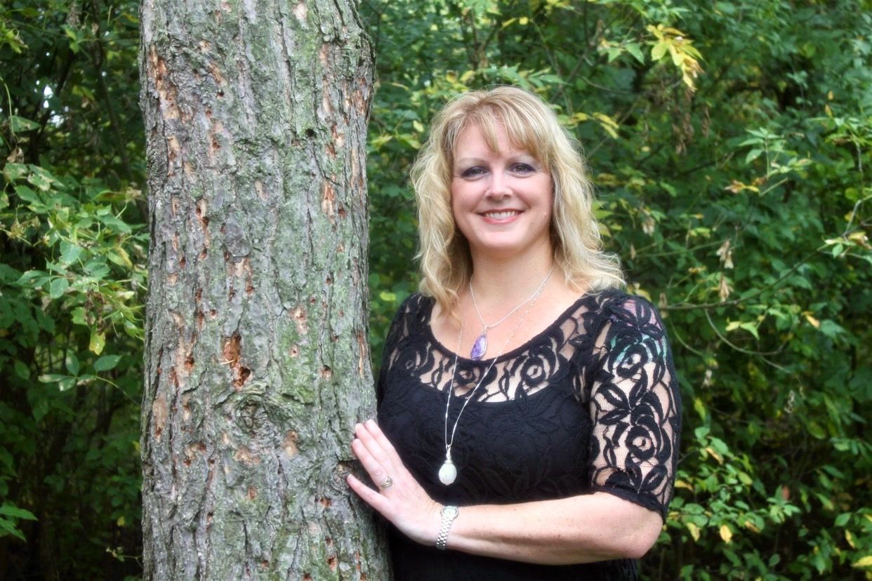 a woman in a black dress is standing next to a tree.
