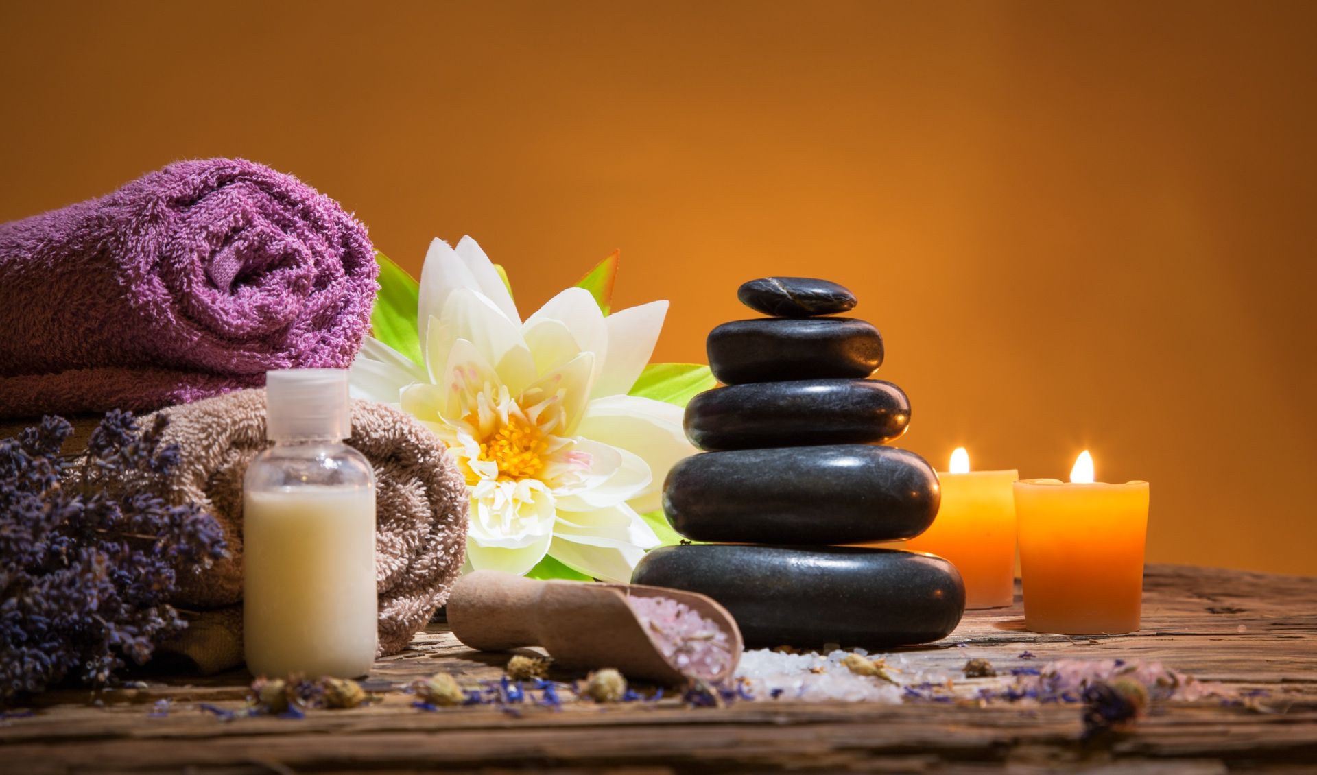 a wooden table topped with towels , candles , rocks and a flower.