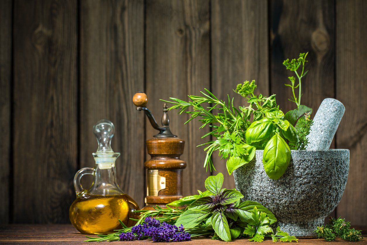 a mortar and pestle filled with herbs and a bottle of oil on a wooden table.