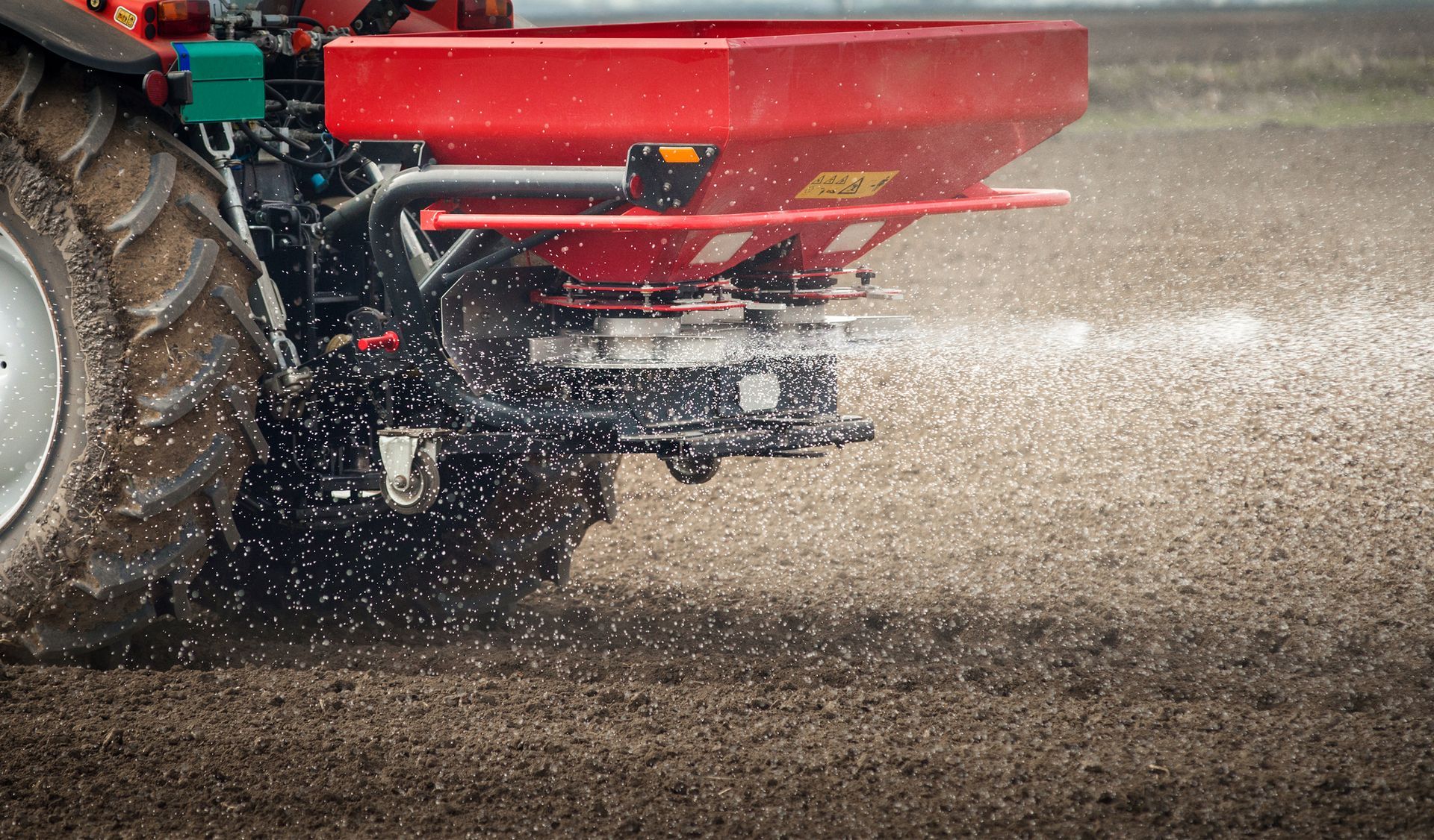 a red tractor is spraying fertilizer on a dirt field