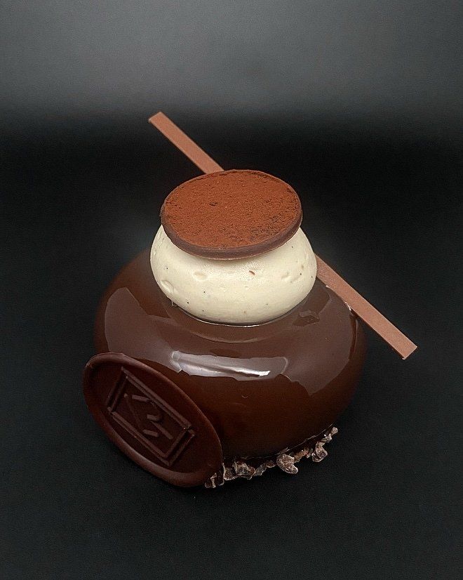 Gâteau à la mousse au chocolat avec glaçage, couche blanche, biscuit au cacao, barre de chocolat et logo sur fond noir.