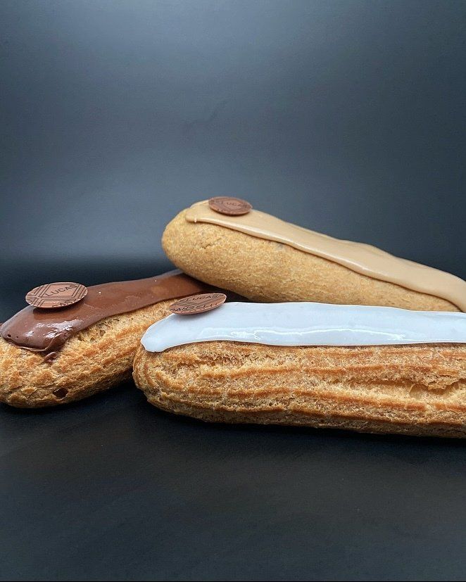 Trois éclairs avec un glaçage de couleurs différentes et une garniture en chocolat sur fond noir.