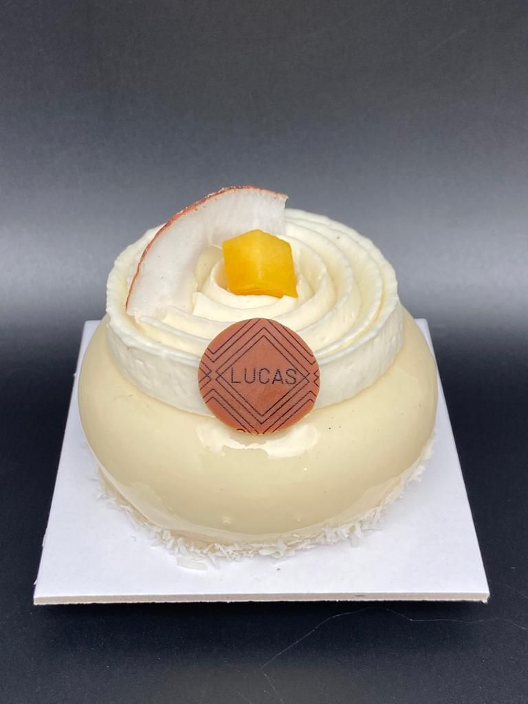 Dessert glacé blanc avec crème fouettée, noix de coco et médaillon de chocolat, sur une assiette carrée blanche.