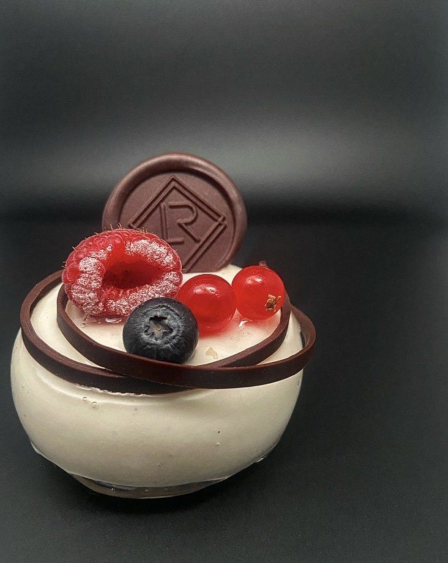 Un petit dessert blanc garni de baies et d'une garniture au chocolat sur un fond sombre.