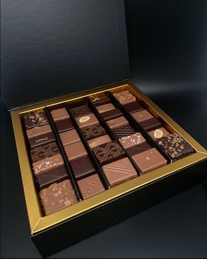 Boîte de chocolats assortis, disposés en rangées, à l'intérieur d'une boîte noire avec bordure dorée.