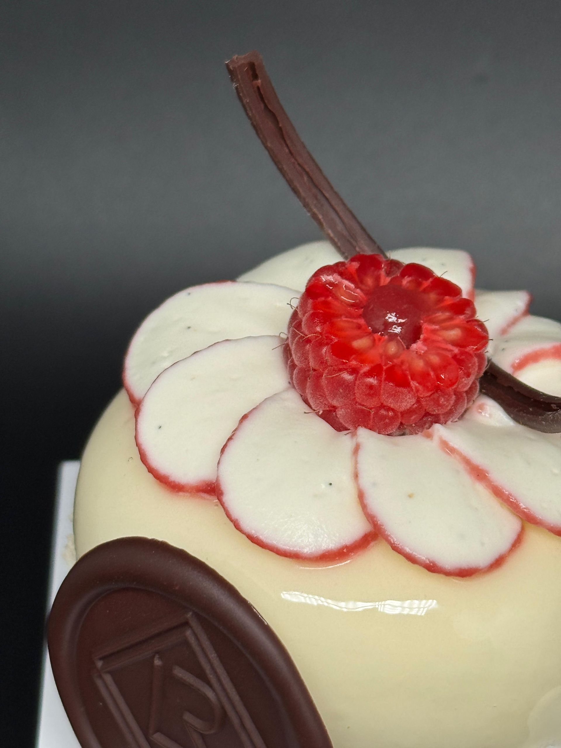 Gâteau glacé blanc, garni d'un chocolat blanc en forme de framboise et de pétale avec des bords rouges, accent de chocolat.