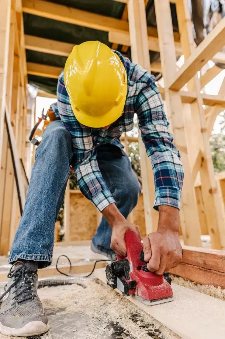 A man wearing a hard hat is using a plane on a piece of wood in San Jose, CA