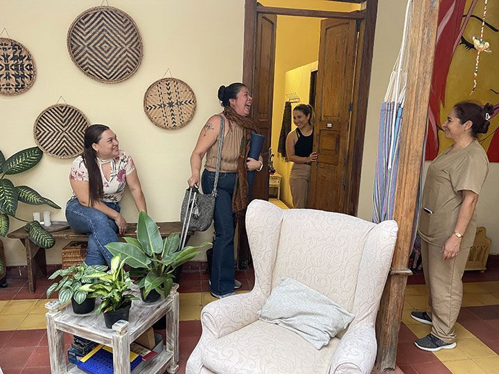 Tres mujeres están paradas alrededor de una silla en una sala de estar.