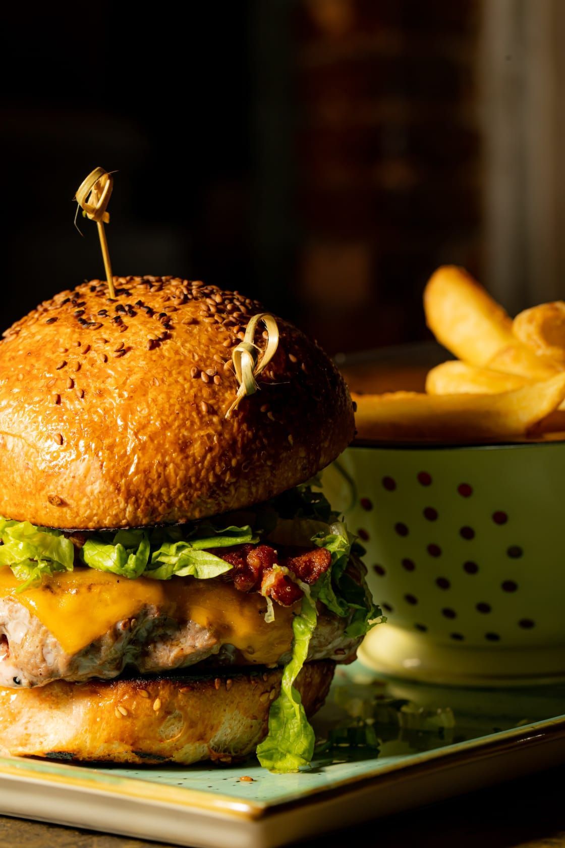 Un hamburger è seduto su un piatto accanto a una ciotola di patatine fritte.