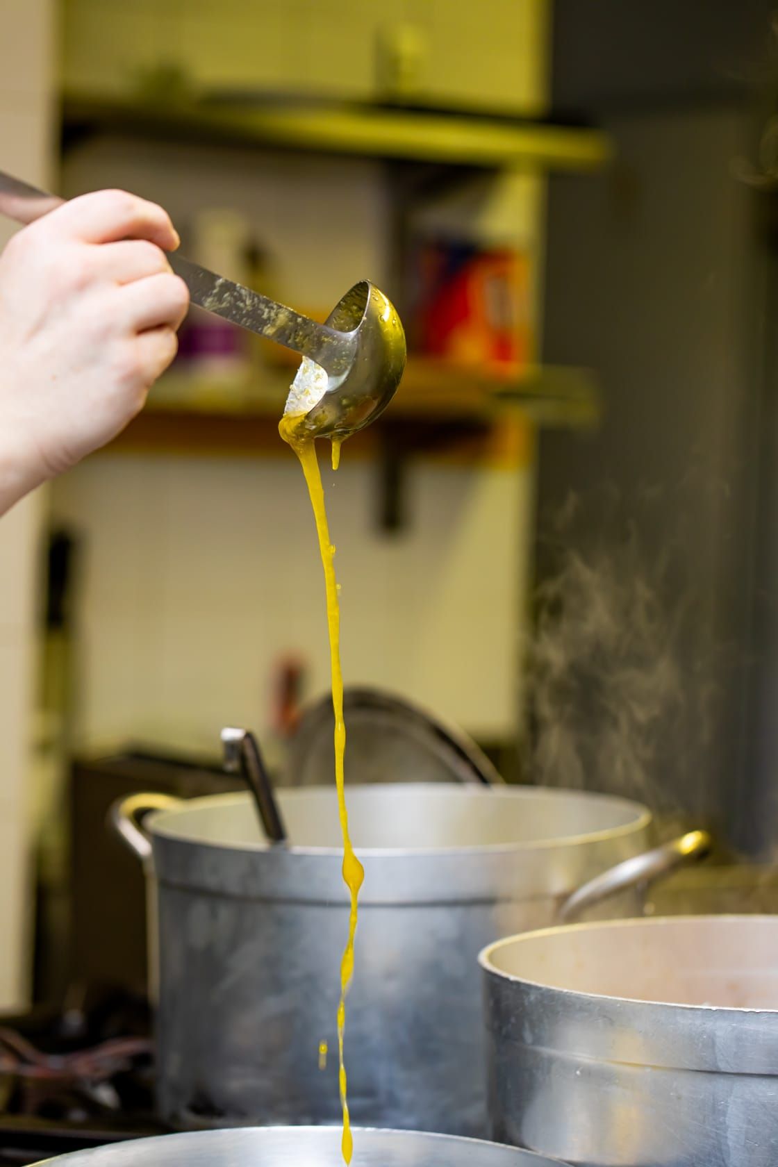Una persona versa la zuppa in una pentola con un mestolo.
